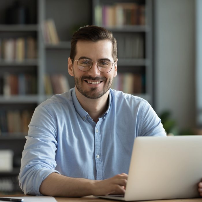 employee in glasses sitting at desk in front of laptop smiling looking at camera